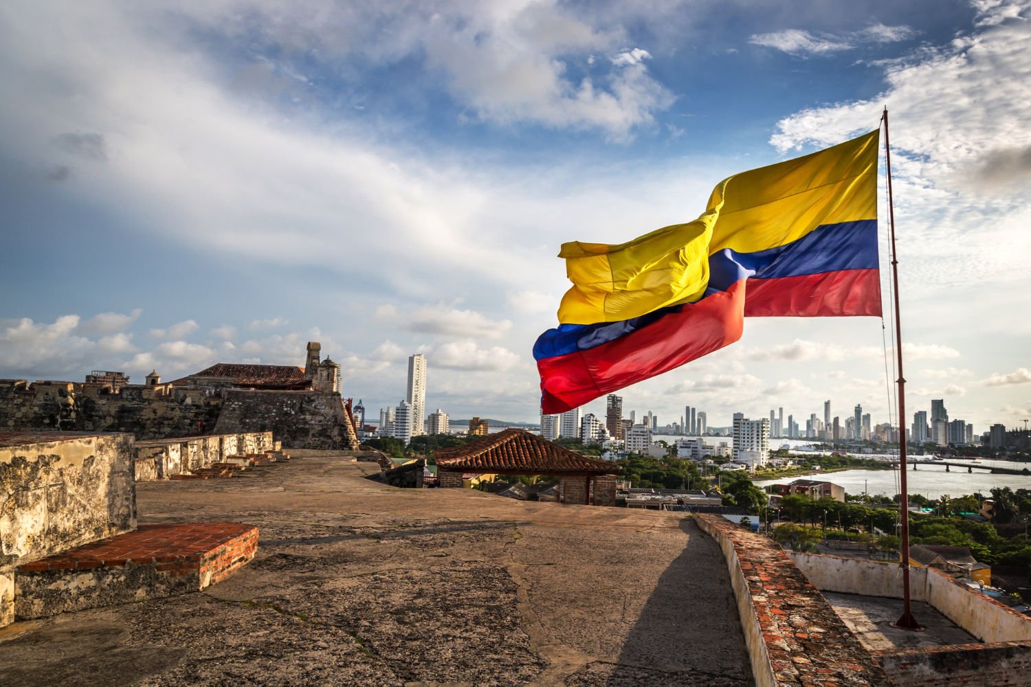 bandera de colombia frente a un cielo azul y una construcción antigua